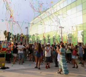 Una multitud de persones al voltant d'un edifici gran amb serpentines de colors